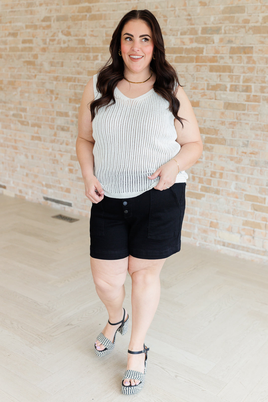 Woman wearing a striped tank top and black shorts against a brick wall.