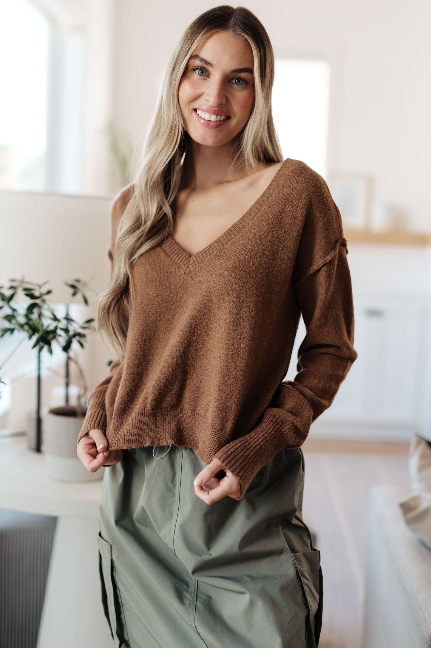 Woman wearing a brown sweater and green pants in a kitchen setting