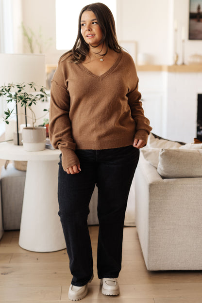 Woman wearing a brown sweater and black pants standing in a living room.