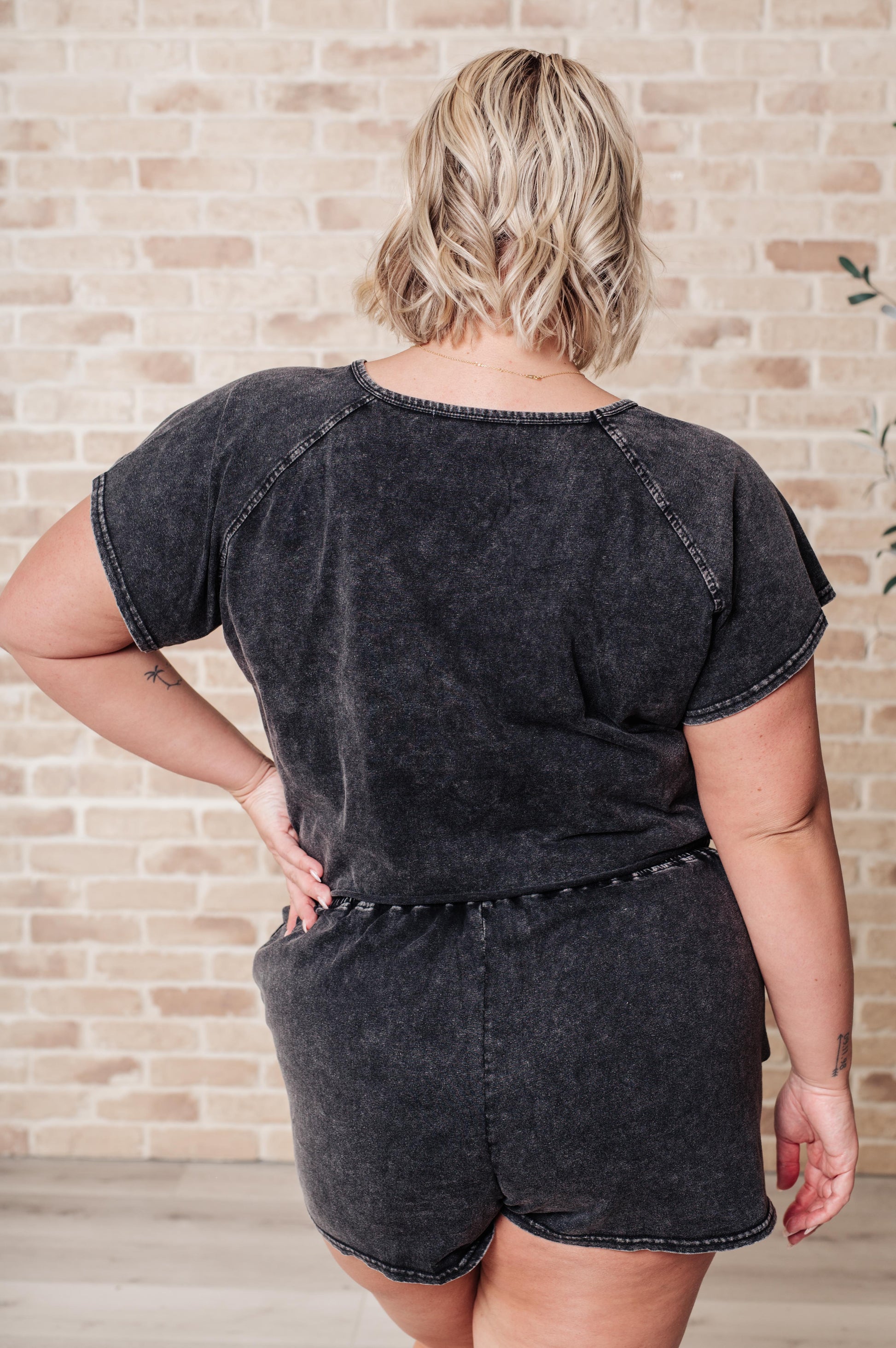 Person wearing a black denim romper against a brick wall.