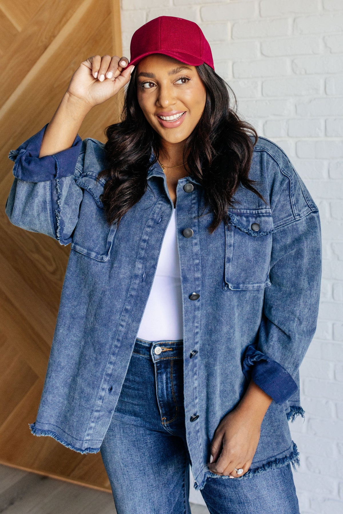 Woman wearing a red cap and denim jacket against a white brick wall.