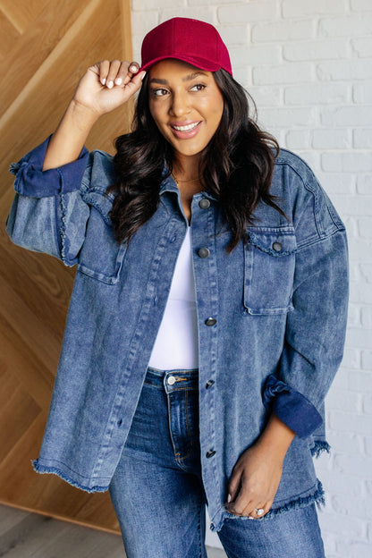 Woman wearing a red cap and denim jacket against a white brick wall.