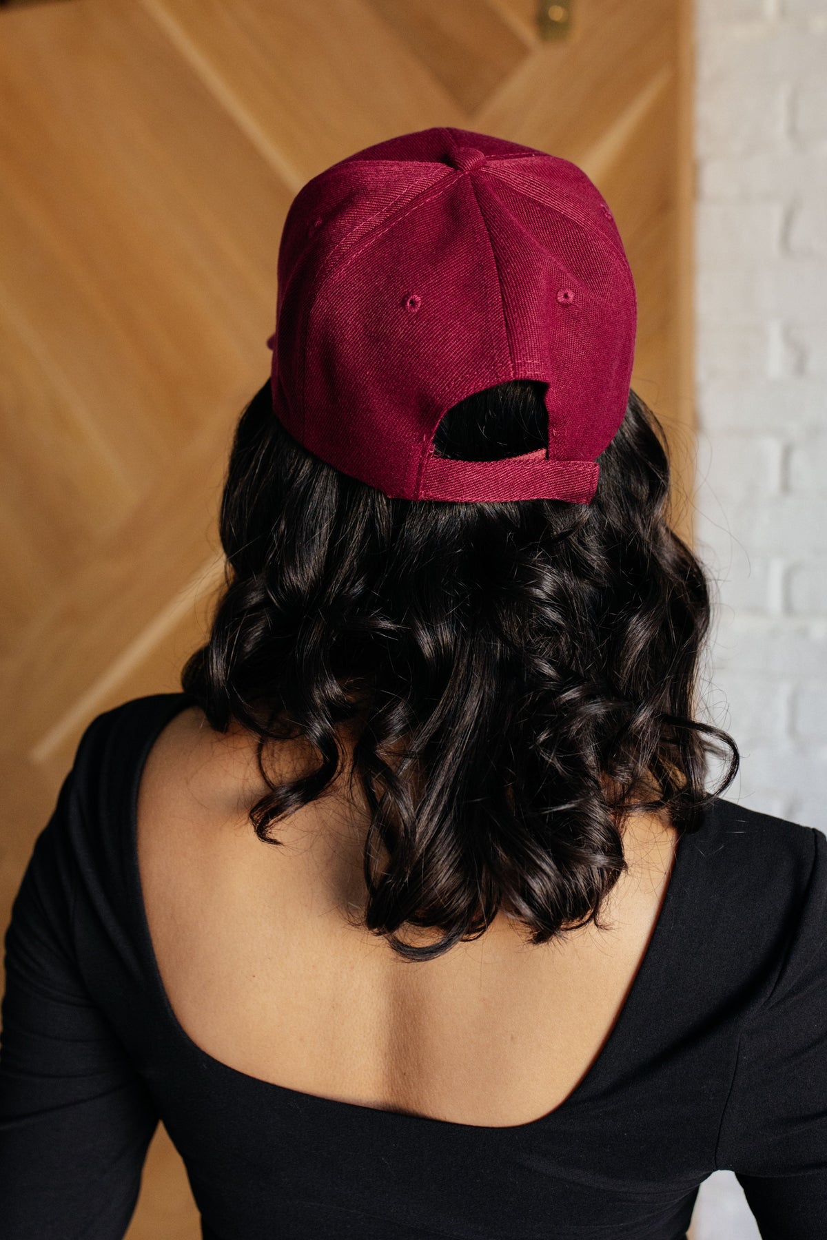 Person wearing a red cap from behind with a wooden door and white wall in the background