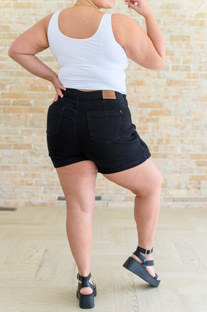 A person wearing a high rise side tie denim skort in black color with a self-tie side closure.