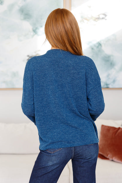 Person wearing a blue sweater in a room with a blurred background