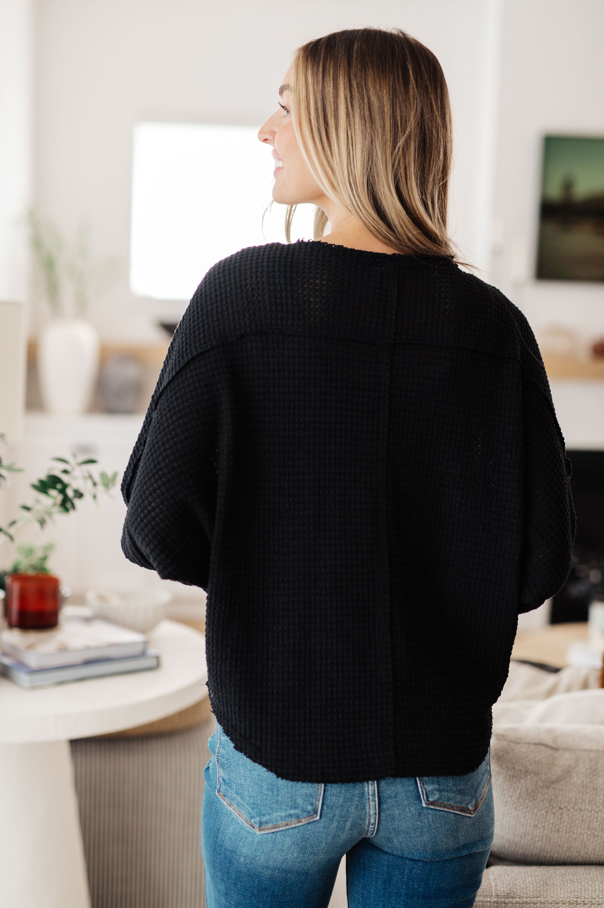 Person wearing a black sweater and blue jeans in a living room setting