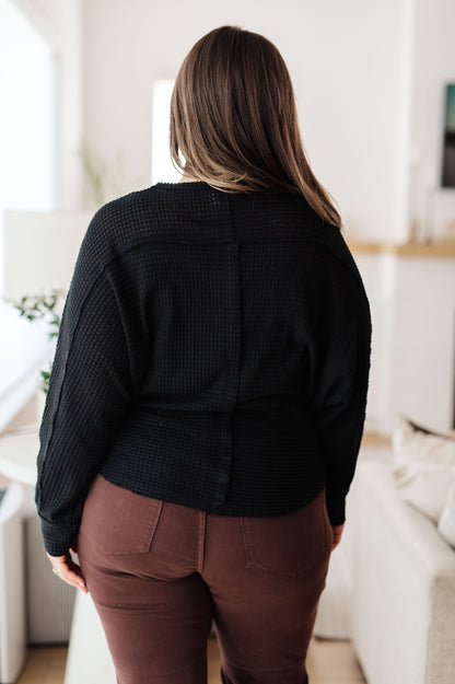 Person wearing a black jacket and brown pants in a room with white walls and furniture.