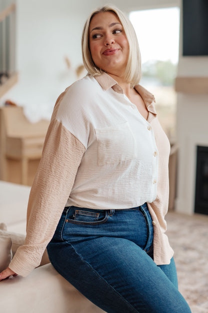 Woman wearing a beige shirt over a white top with blue jeans in a living room.