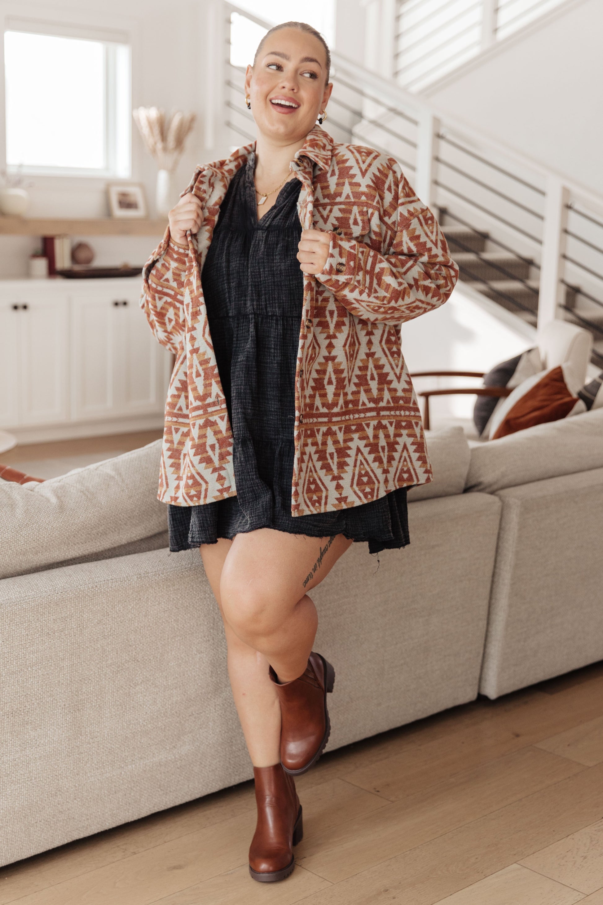 Woman in a patterned jacket and black dress standing in a living room.