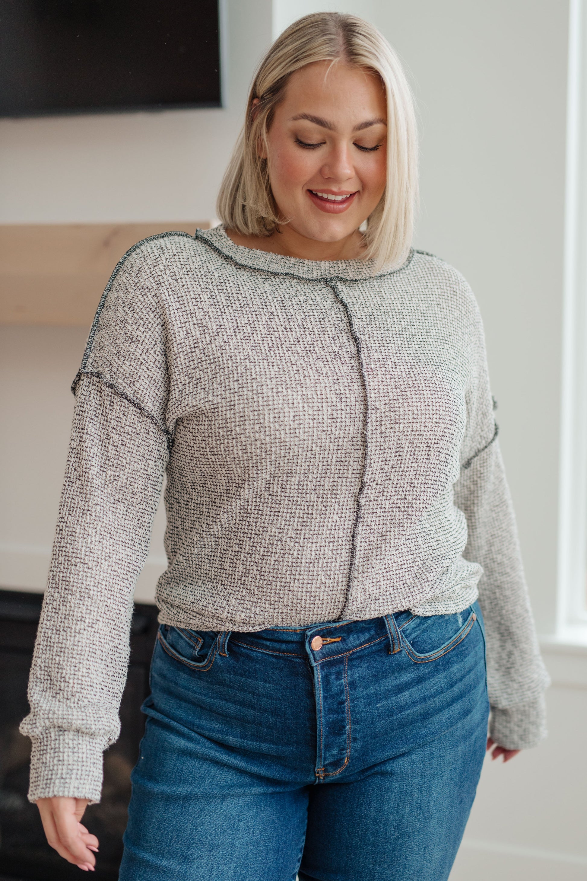 Woman wearing a gray sweater and blue jeans indoors
