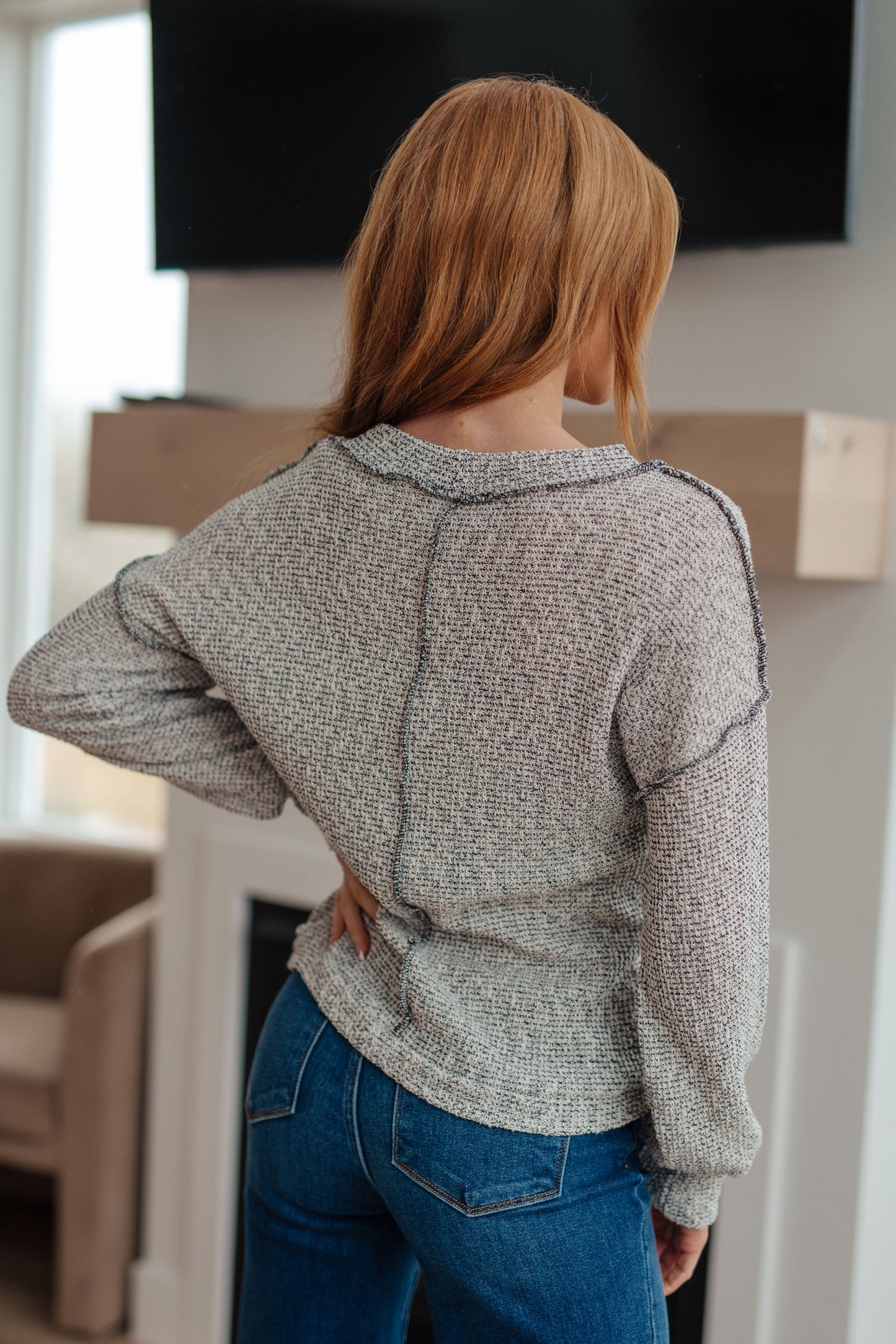 Person wearing a gray sweater and blue jeans standing indoors.