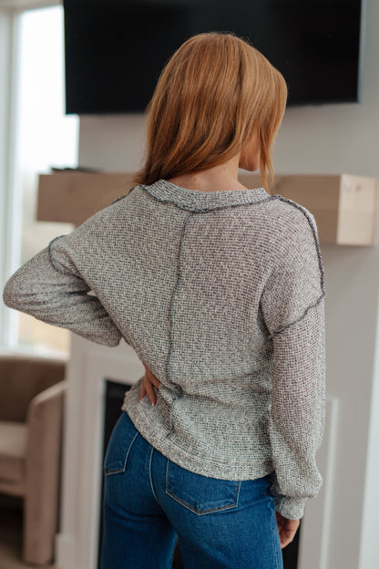 Person wearing a gray sweater and blue jeans standing indoors.