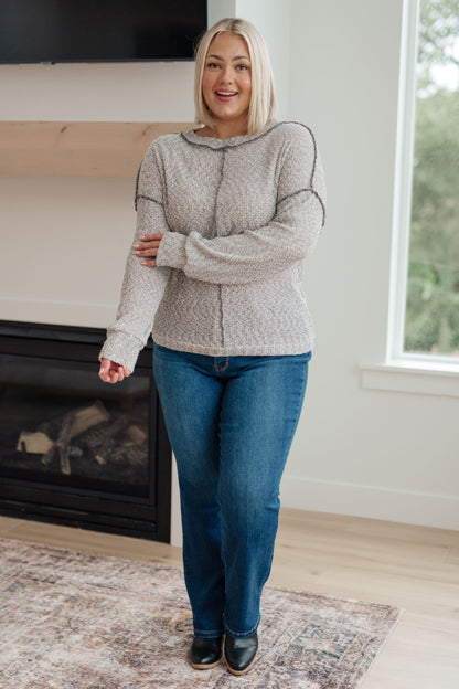 Woman wearing a patterned sweater and blue jeans standing in a room with a fireplace and window.