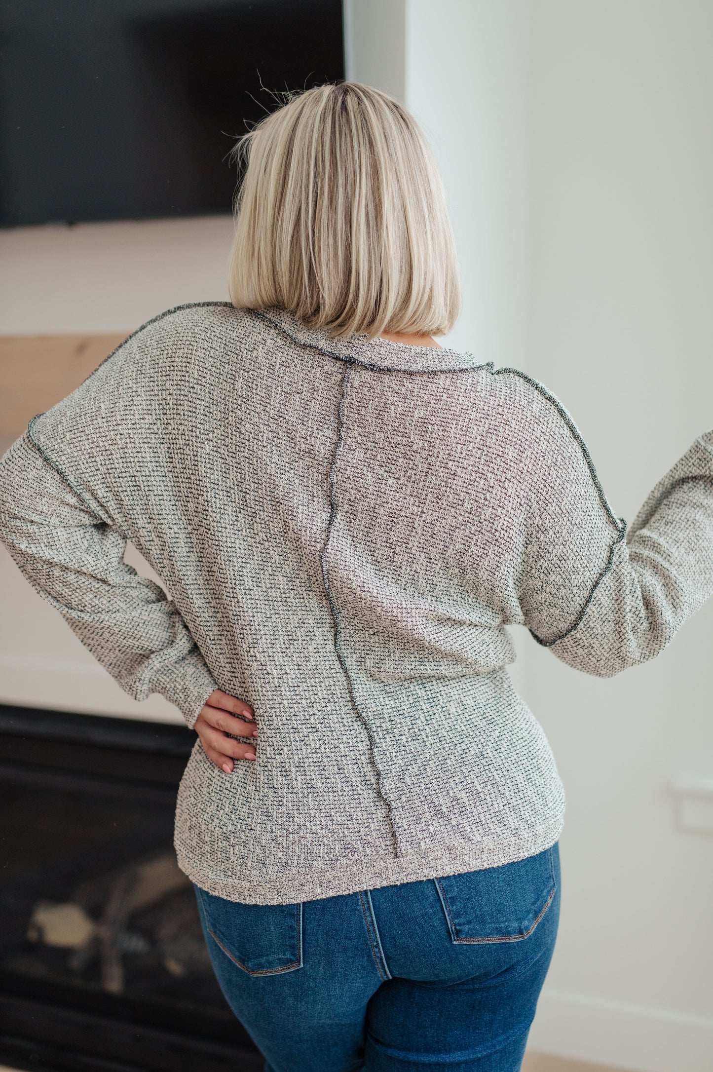 Person wearing a textured gray sweater and blue jeans in an indoor setting