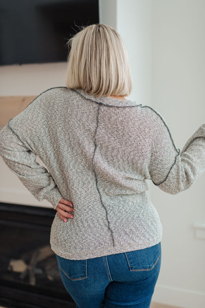 Person wearing a textured gray sweater and blue jeans in an indoor setting