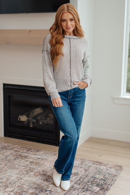 Woman wearing a gray sweater and blue jeans standing in a room with a fireplace.