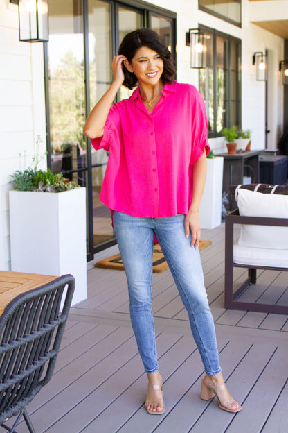 Woman in a bright pink shirt and blue jeans standing on a patio.