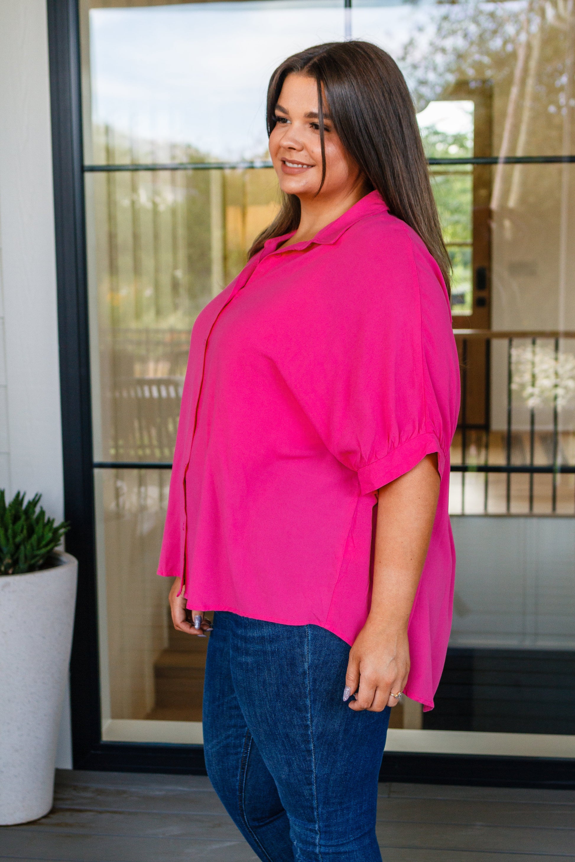 Woman wearing a bright pink blouse and blue jeans standing indoors.