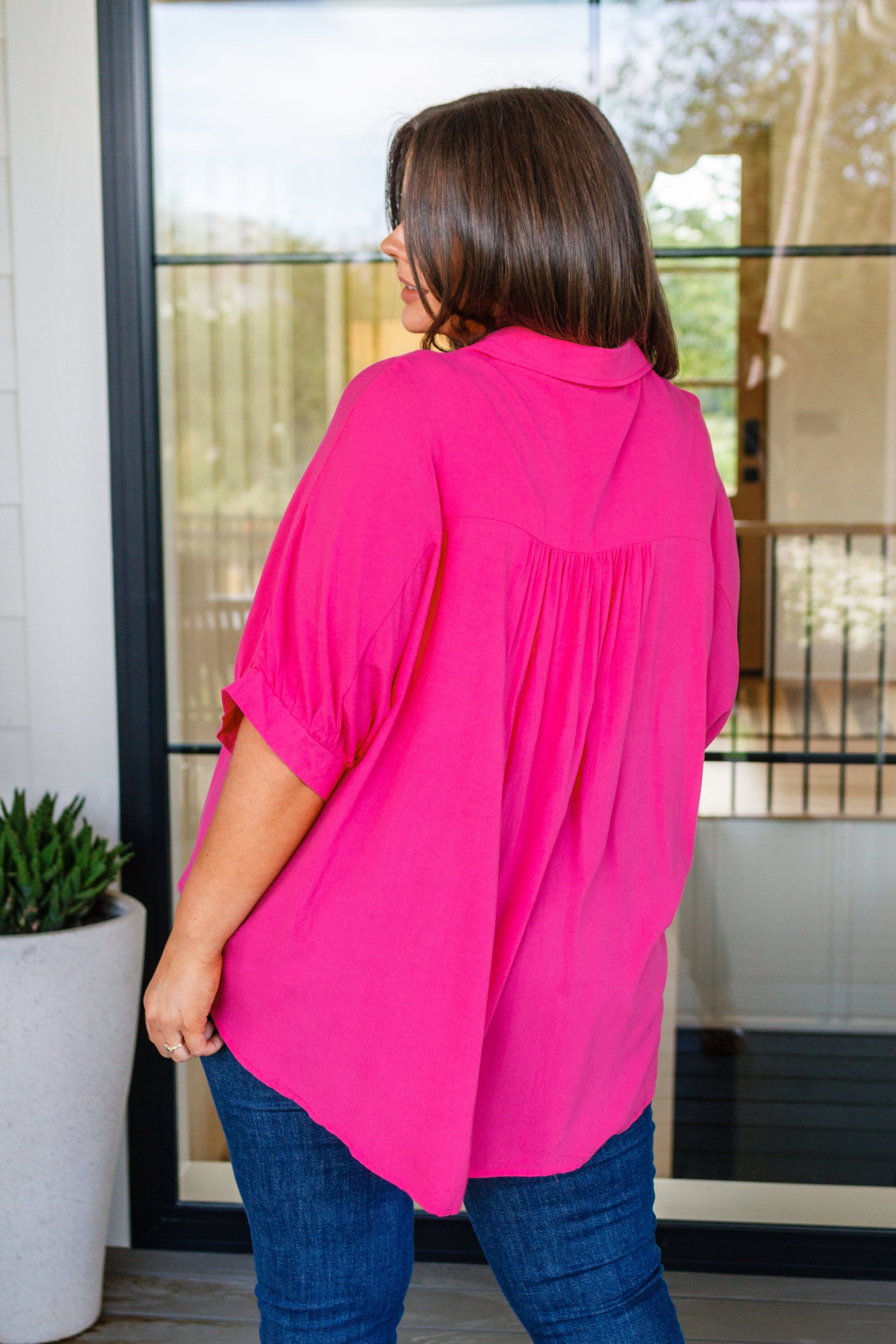 Person wearing a bright pink blouse standing in a room with a glass door.