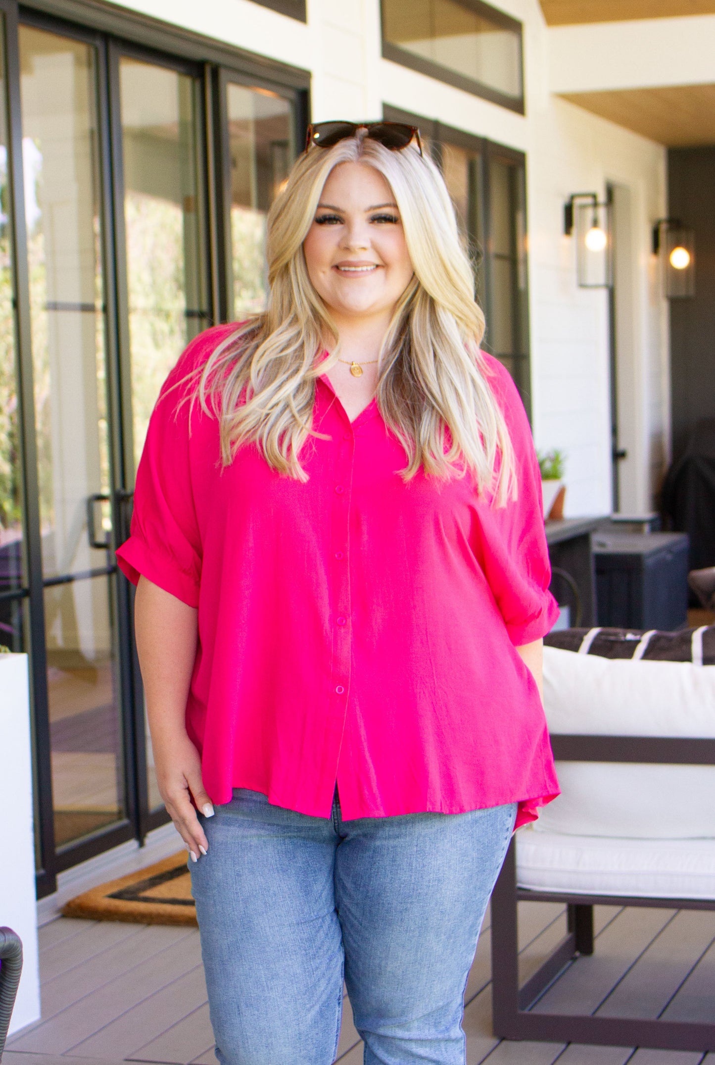 Woman wearing a bright pink blouse and blue jeans standing outdoors.