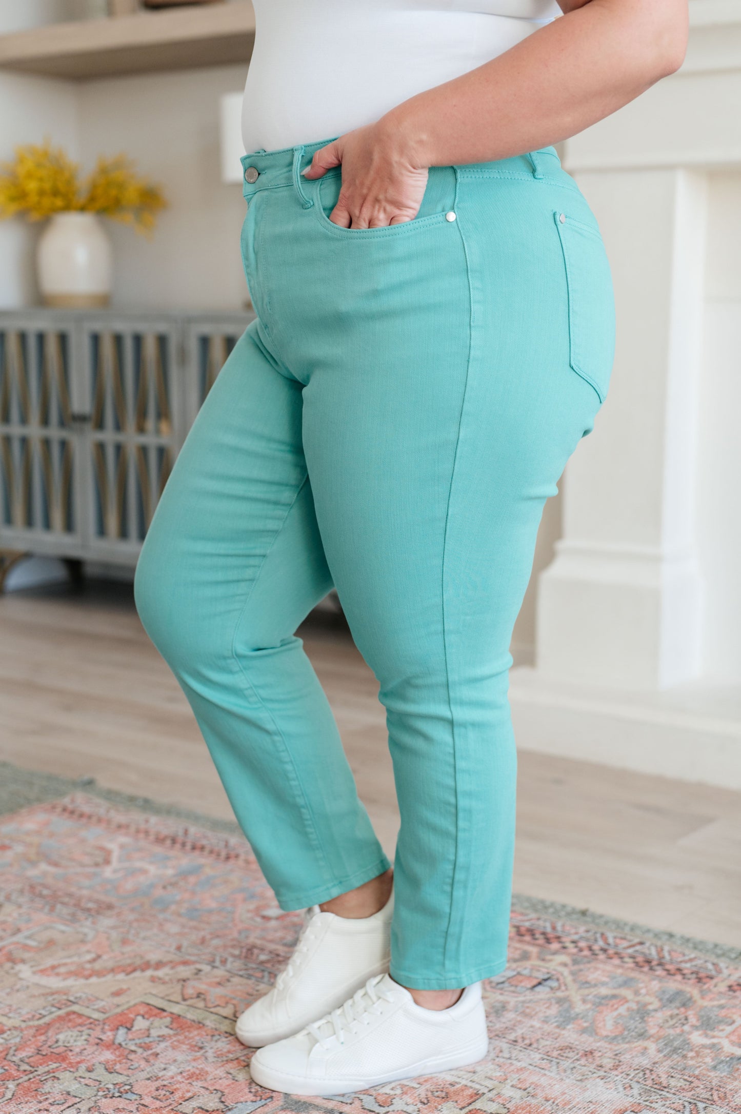 Person wearing turquoise jeans and white sneakers in a home setting
