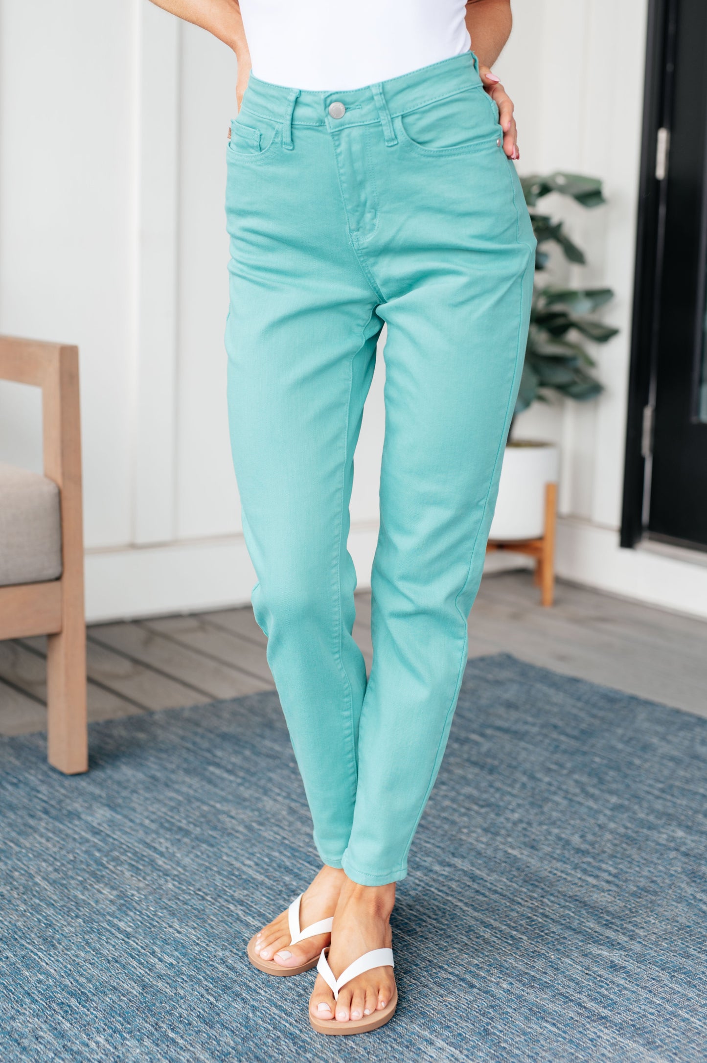 Person wearing turquoise jeans standing on a blue rug indoors.