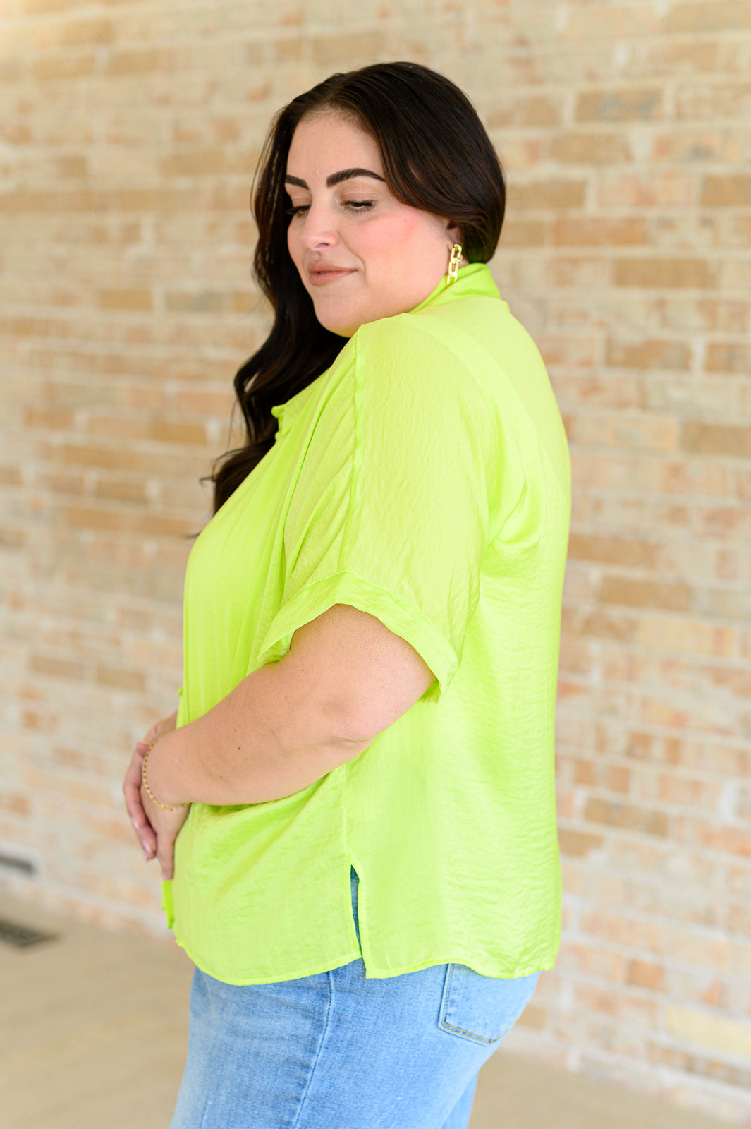 A woman wearing a bright citrus yellow button down blouse with short sleeves, paired with a white top and blue jeans.