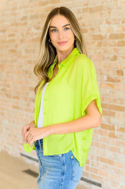 A woman wearing a bright citrus yellow button down blouse with short sleeves, paired with a white top and blue jeans.