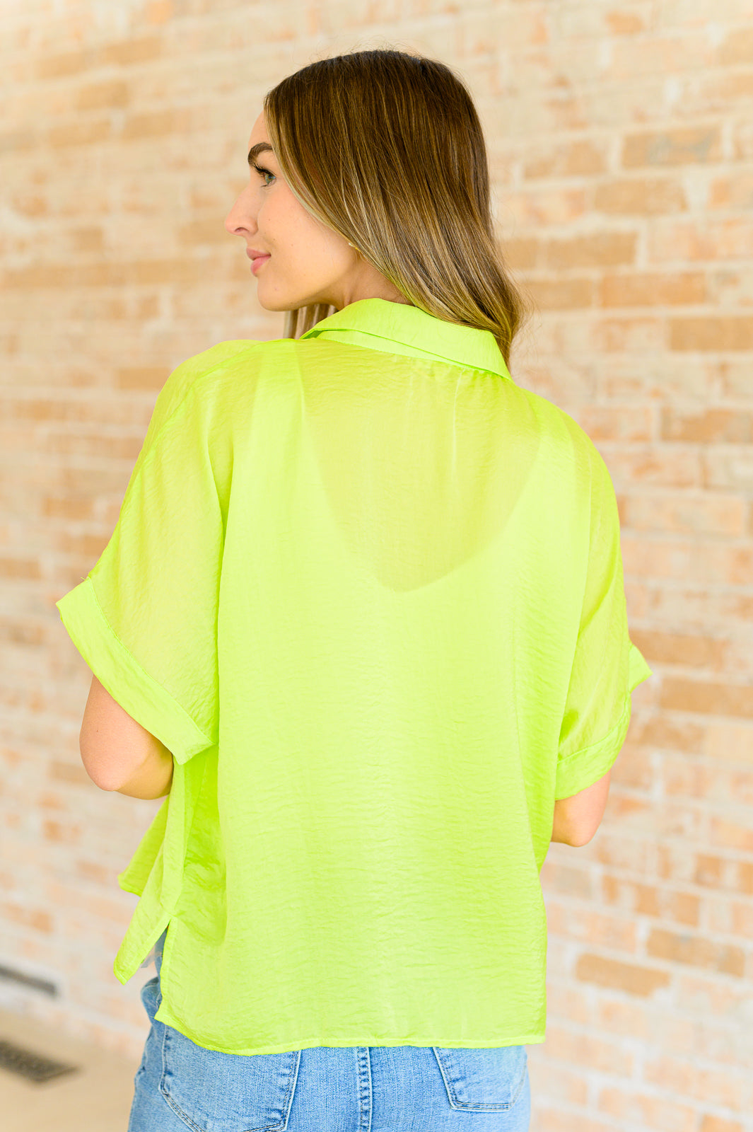 A woman wearing a bright citrus yellow button down blouse with short sleeves, paired with a white top and blue jeans.