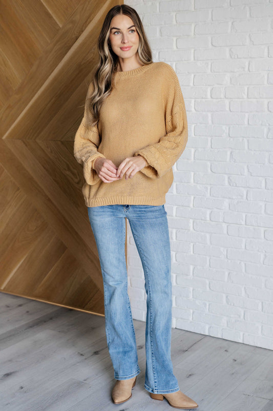 Woman wearing a mustard yellow sweater and blue jeans standing against a white brick wall.