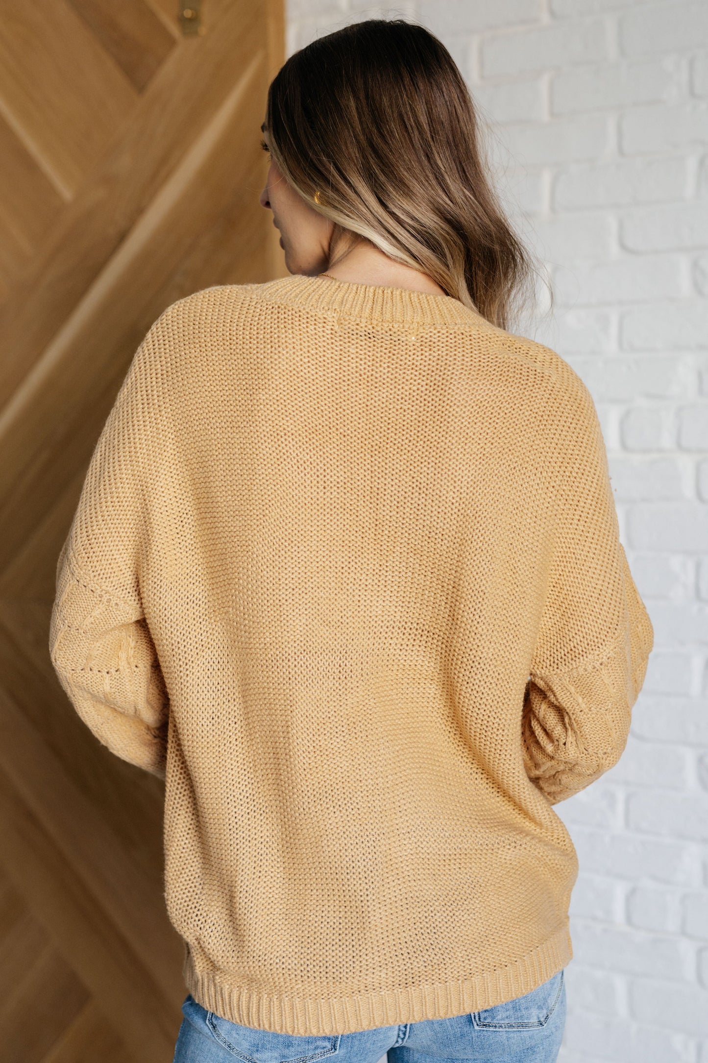 Woman wearing a mustard yellow sweater standing against a white brick wall.