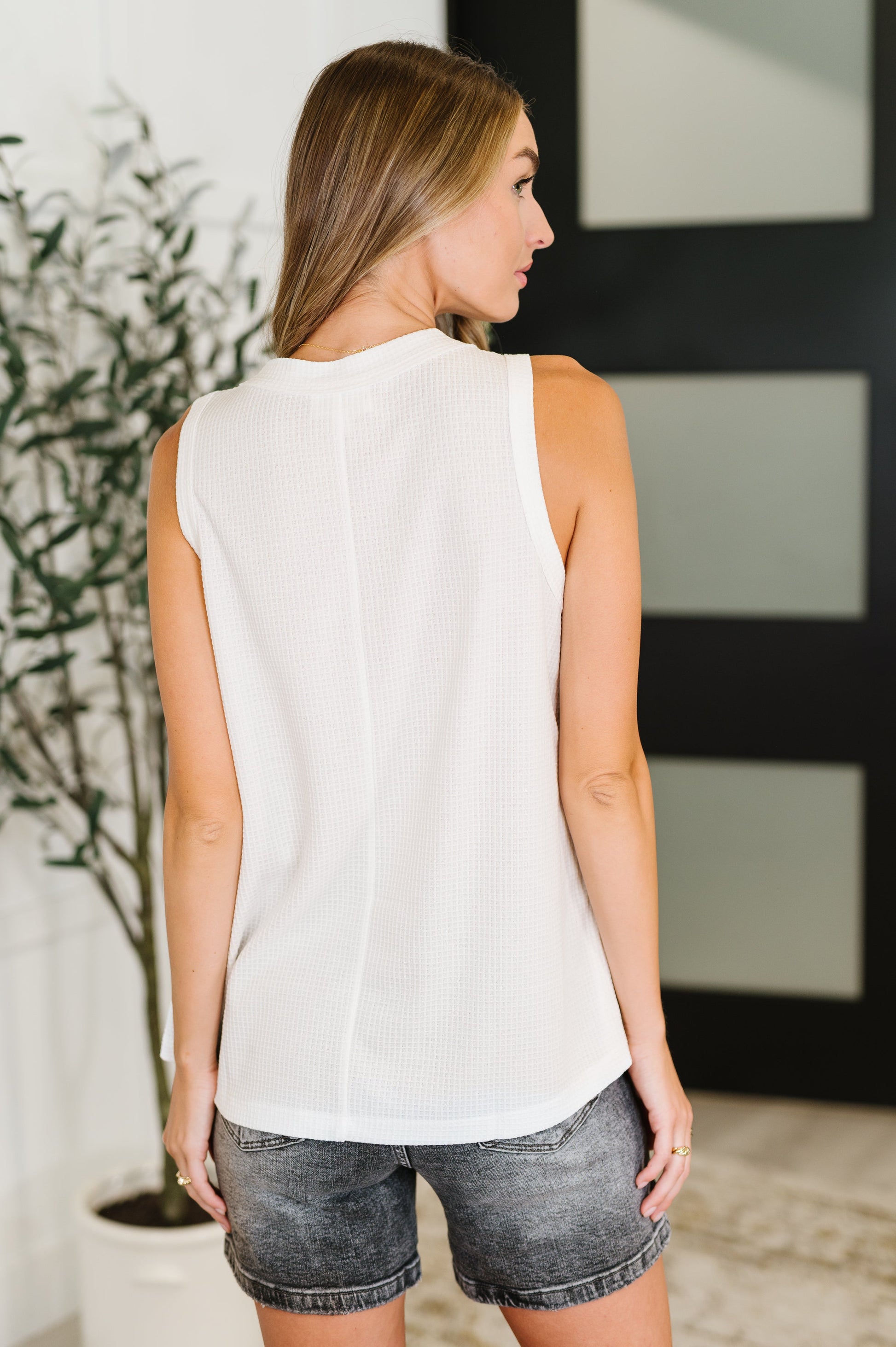 Woman wearing a white sleeveless top and denim shorts in an indoor setting.