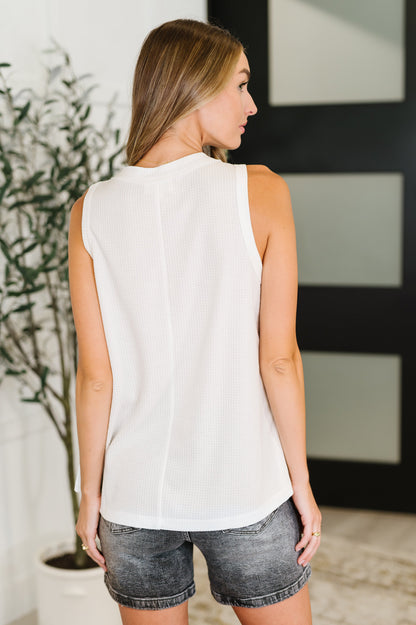 Woman wearing a white sleeveless top and denim shorts in an indoor setting.