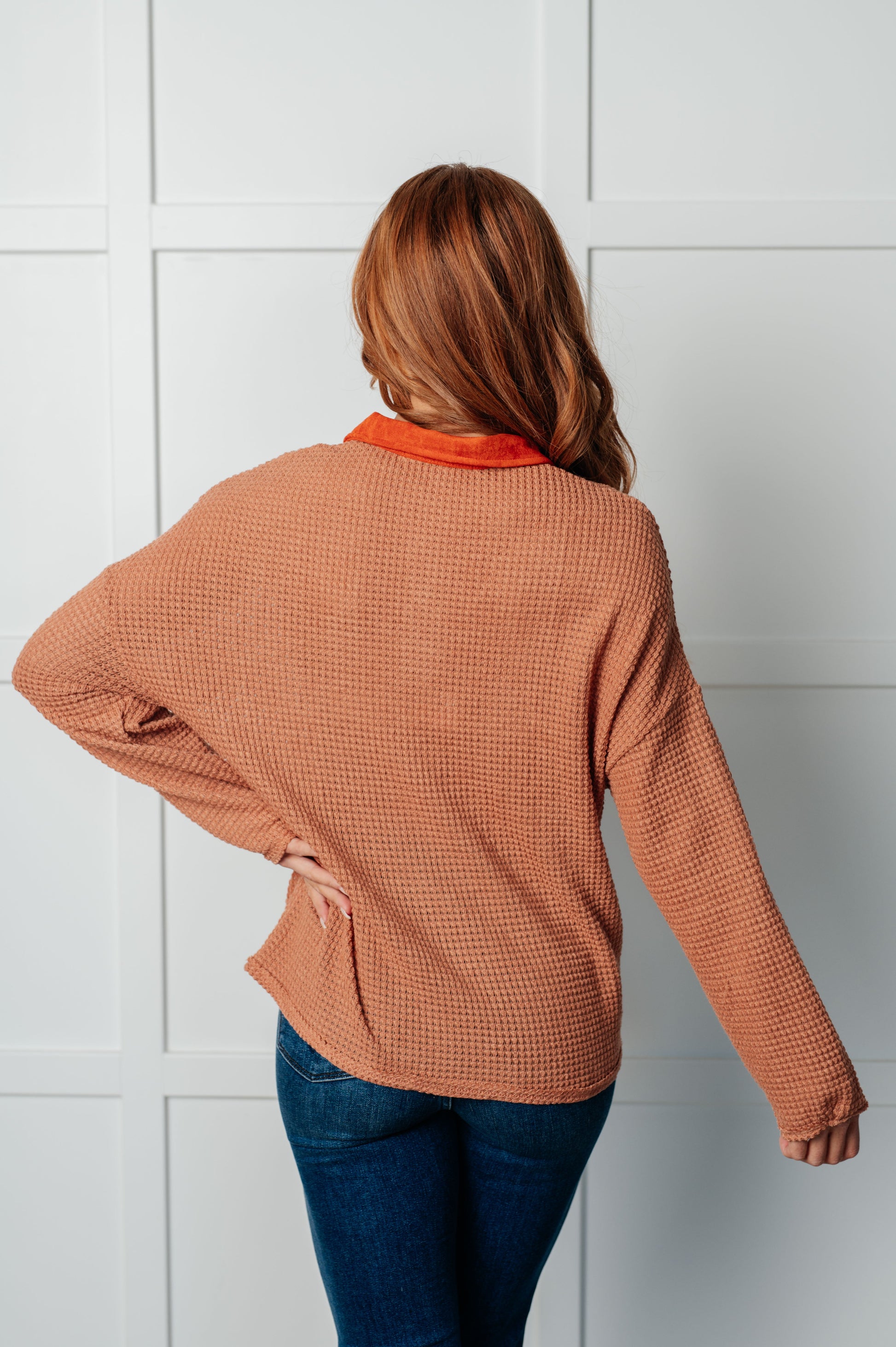 Person wearing a brown checkered jacket and blue jeans against a white tiled wall.