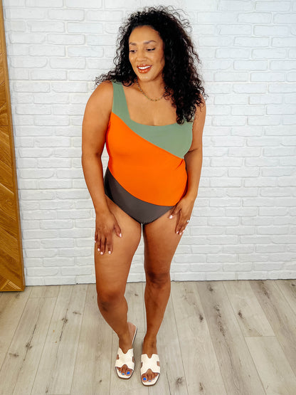 Woman wearing a colorful swimsuit standing against a white brick wall.