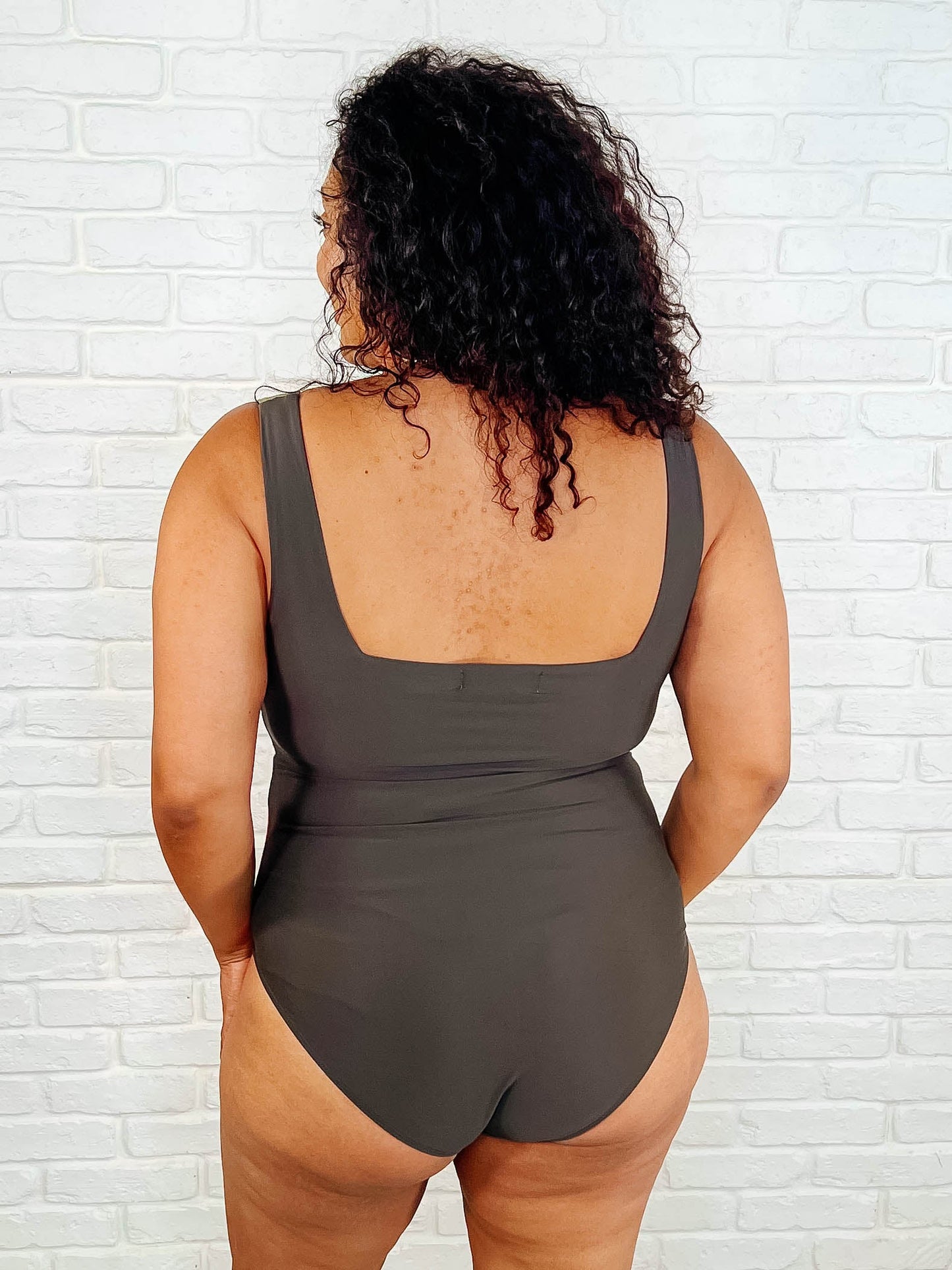 Person wearing a brown swimsuit against a white brick wall.