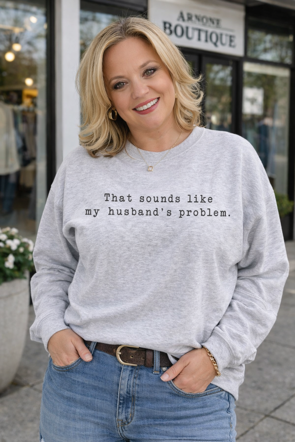 Woman wearing a gray sweatshirt with text standing in front of a store.