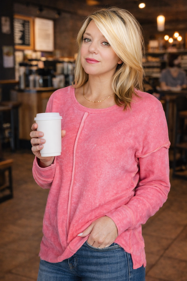 Woman in a pink sweater holding a coffee cup in a coffee shop.