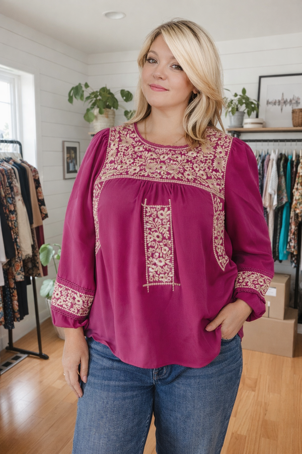 Woman wearing a pink blouse with intricate embroidery in a clothing store.