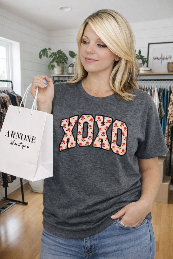 Woman wearing a gray t-shirt with 'XOXO' design, holding a shopping bag in a store.