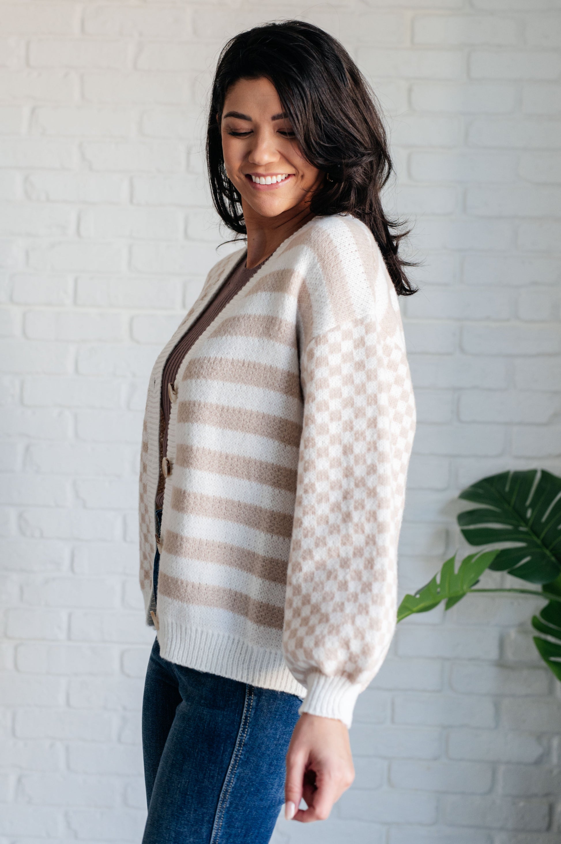 Woman wearing a patterned sweater standing against a white brick wall.