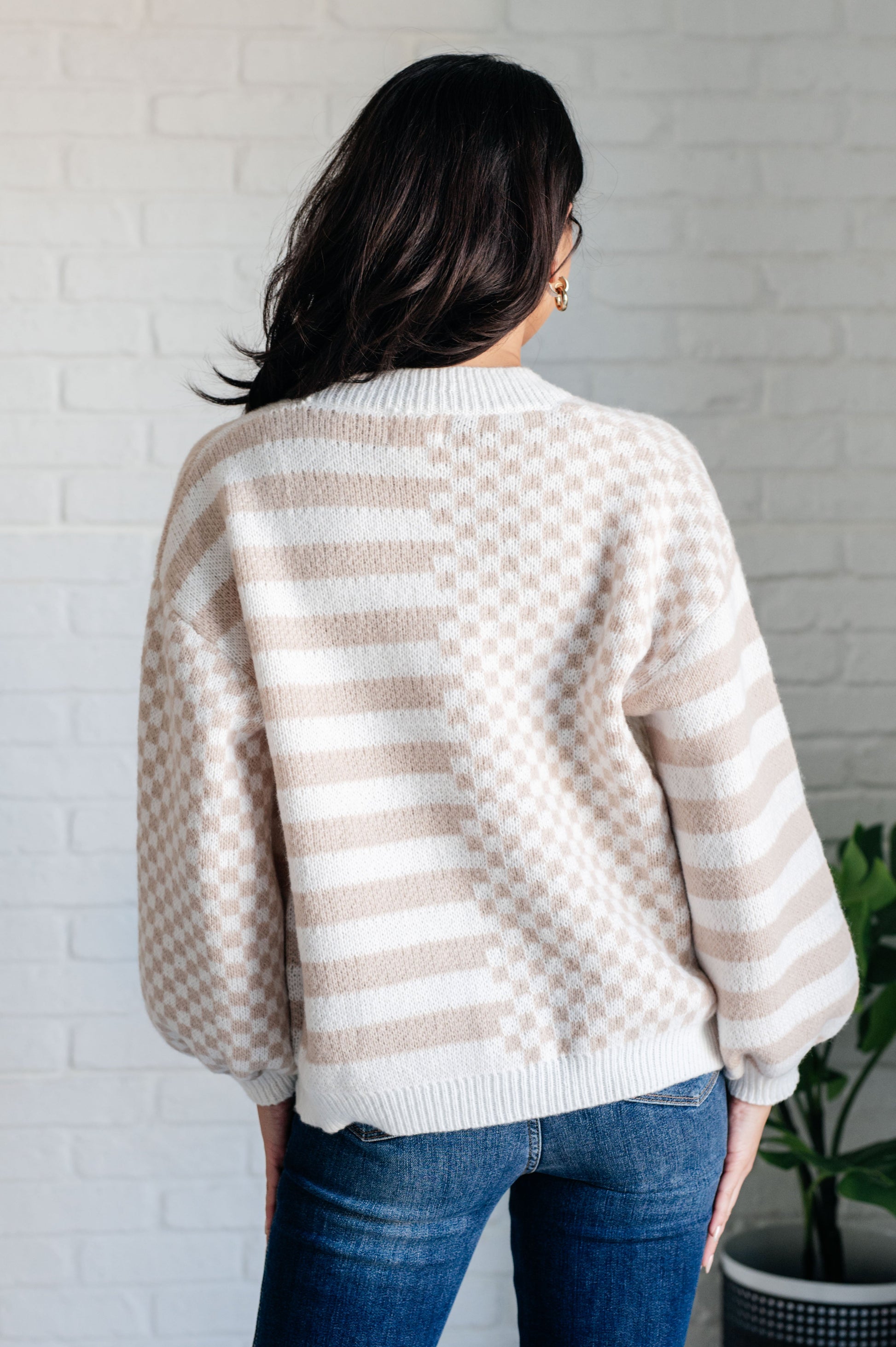 Person wearing a beige and white striped sweater in front of a white brick wall.