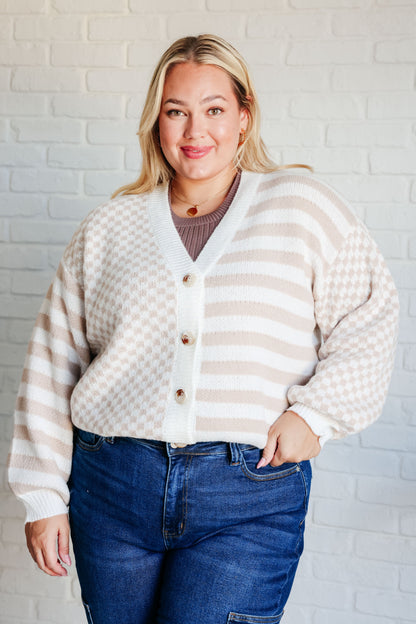 Woman wearing a striped cardigan and jeans against a white brick wall