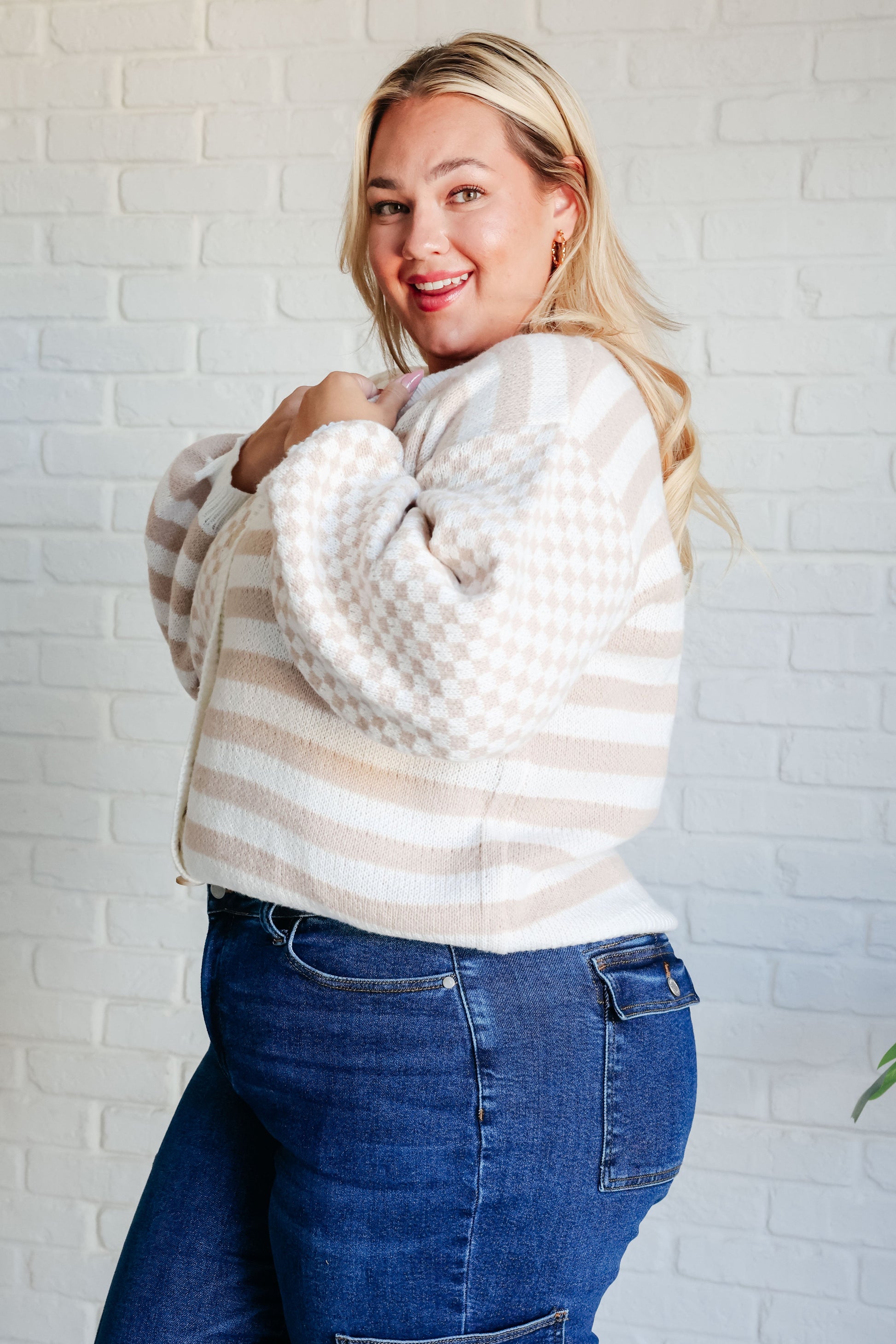 Woman wearing a striped sweater and blue jeans against a white brick wall.