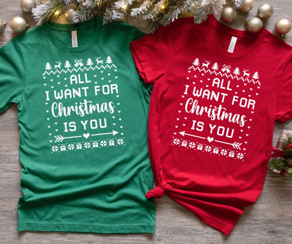 Two Christmas-themed t-shirts, one green and one red, with a festive design on a wooden surface.