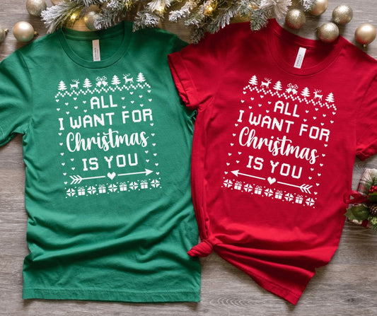 Two Christmas-themed t-shirts, one green and one red, with a festive design on a wooden surface.