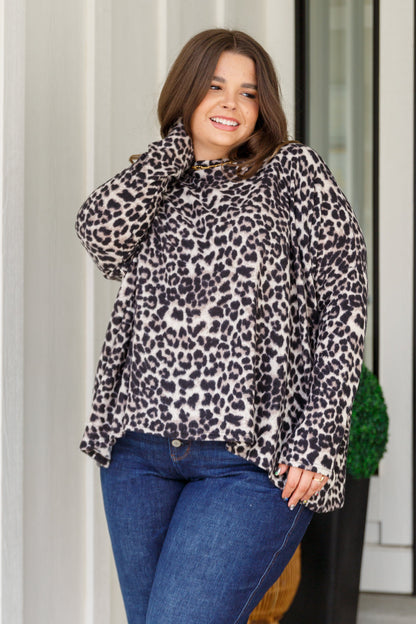Woman wearing a leopard print top and blue jeans standing outdoors.