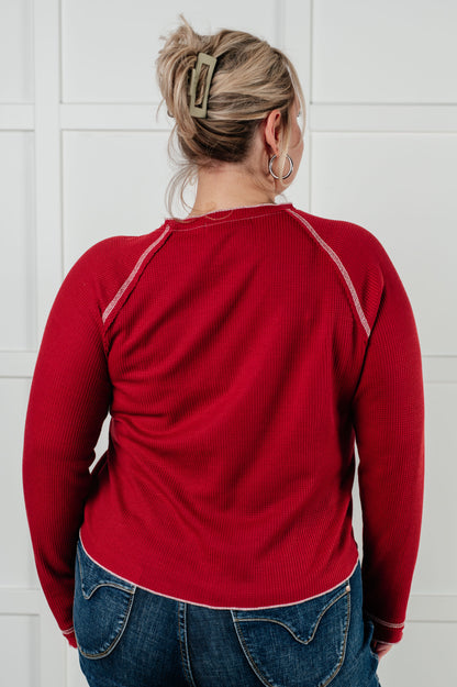 Person wearing a red long-sleeve shirt and blue jeans against a white tiled wall.