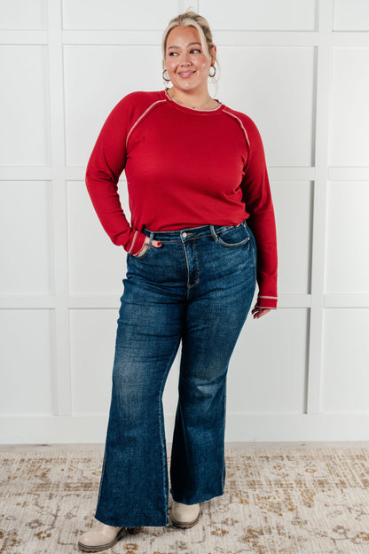 Person wearing a red long-sleeve shirt and blue jeans standing against a white brick wall.