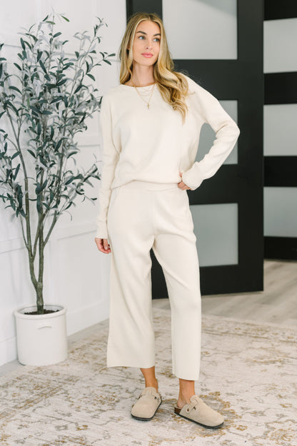 Woman in a white outfit standing in a room with a plant and black and white wall.